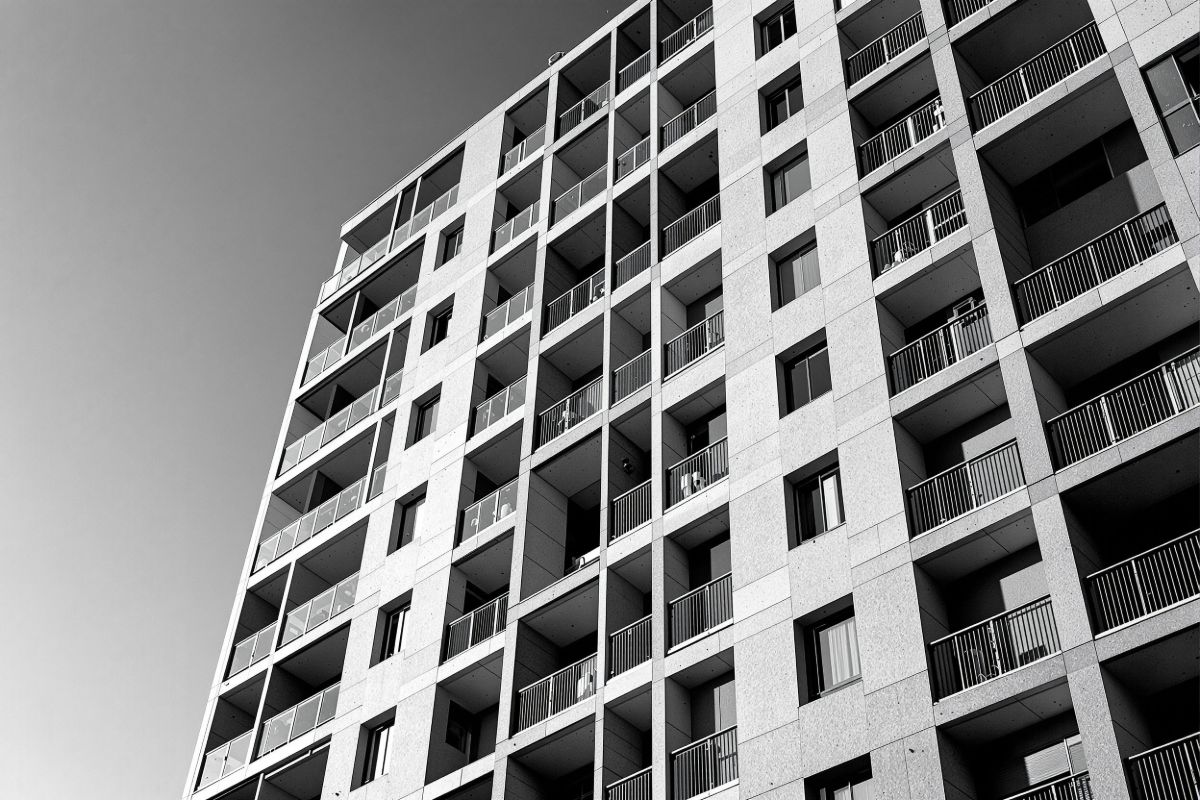 Fachada de un edificio de viviendas recién terminado en ángulo bajo, con la
              retícula de balcones marcada por la luz rasante de la tarde.