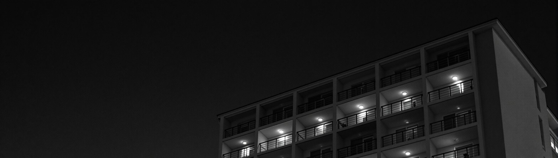 Facade of a 1970s modernist hotel at dusk, warm light spilling from the rooms
        onto the balconies.